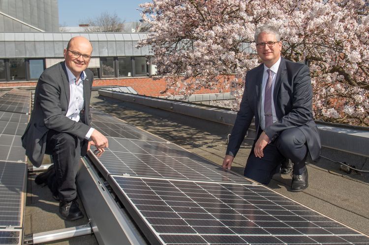 Mr Möllers and Mr Stahlmann kneel on the roof of the university next to a newly installed PV module.