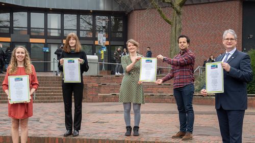 Five people stand in front of the canteen and hold certificates in front of them.