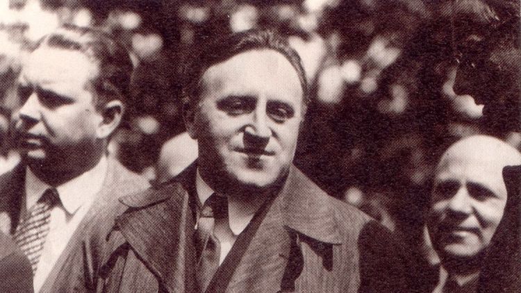 The picture shows Carl von Ossietzky next to other men. He is wearing a suit, tie and coat.