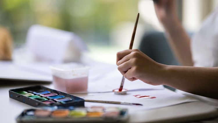 Ein Schulkind trägt Farben aus einem Tuschkasten auf Papier auf.