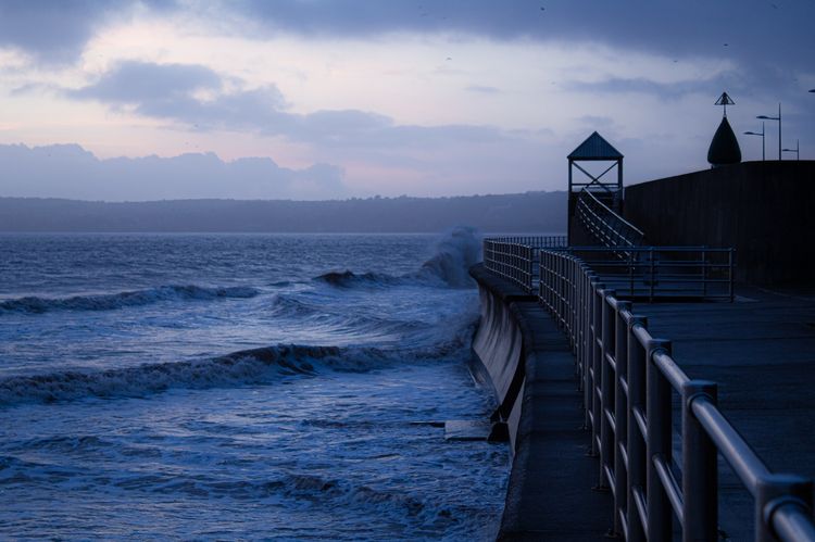 Shows a pier by the sea with waves.